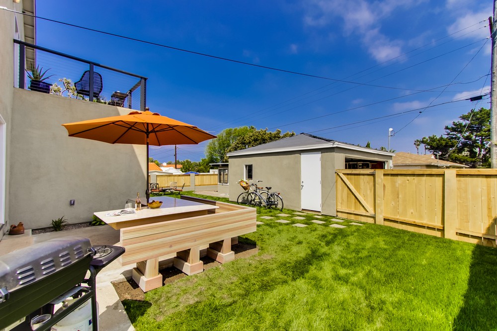 Nicely landscaped backyard with a gas BBQ, detached garage, umbrella, and a large outdoor seating area