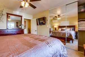 Bedroom with king size bed, ceiling fan, TV, dresser with mirror, AC unit, lamps, mirrored closet for additional storage