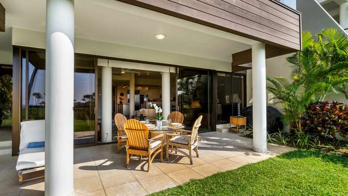 The large lanai has a circular glass table, teak dining chairs, and teak chaise loungers