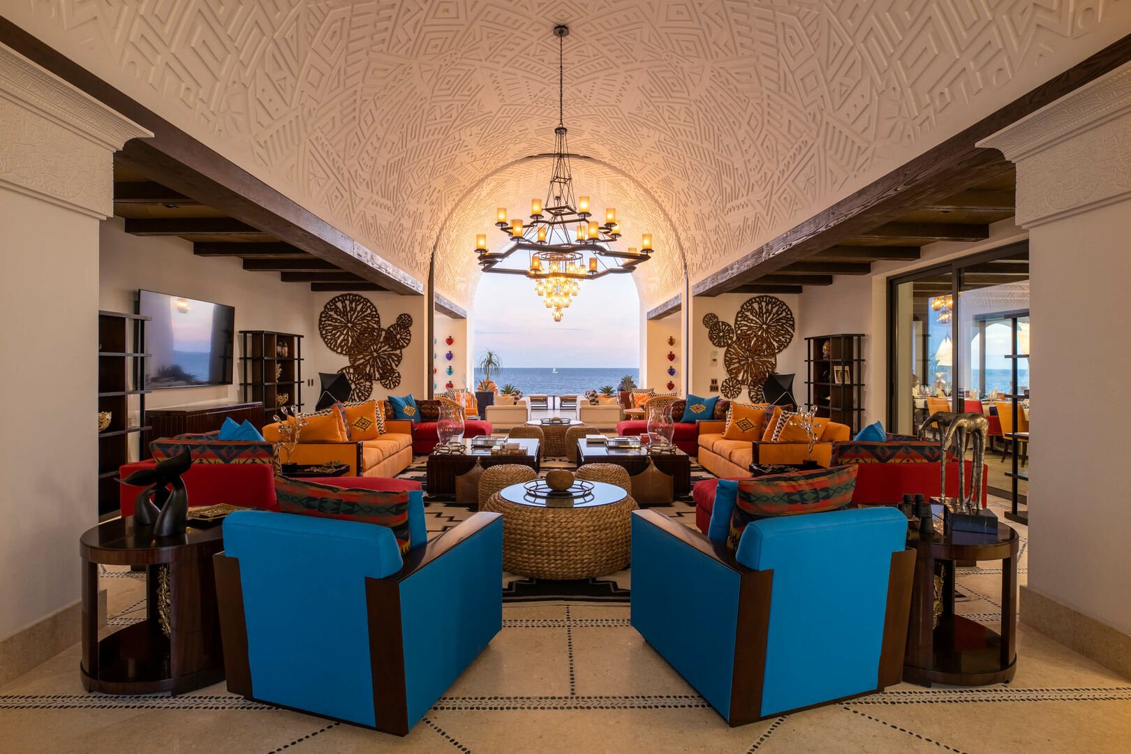 A large sitting area in this Los Cabos beachfront villa, filled with blue, orange, and red chairs and couches, with beach views.