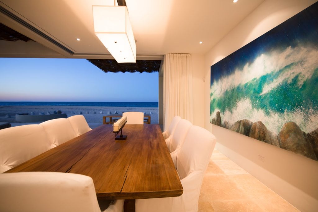 The dining area with white chairs and a large wave painting behind it.