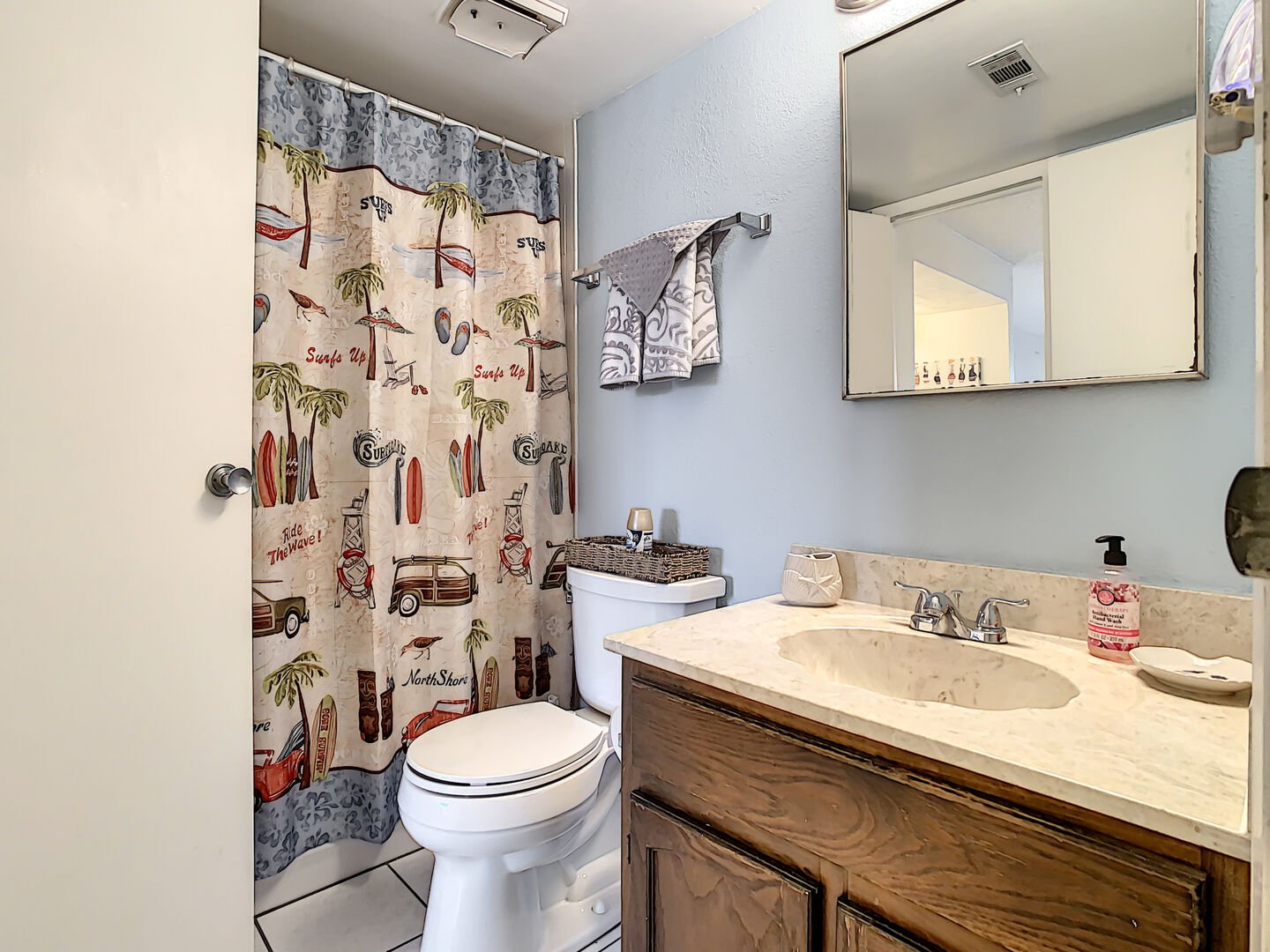 Bathroom with beach-themed shower curtain next to toilet and tan counter with built-in sink.