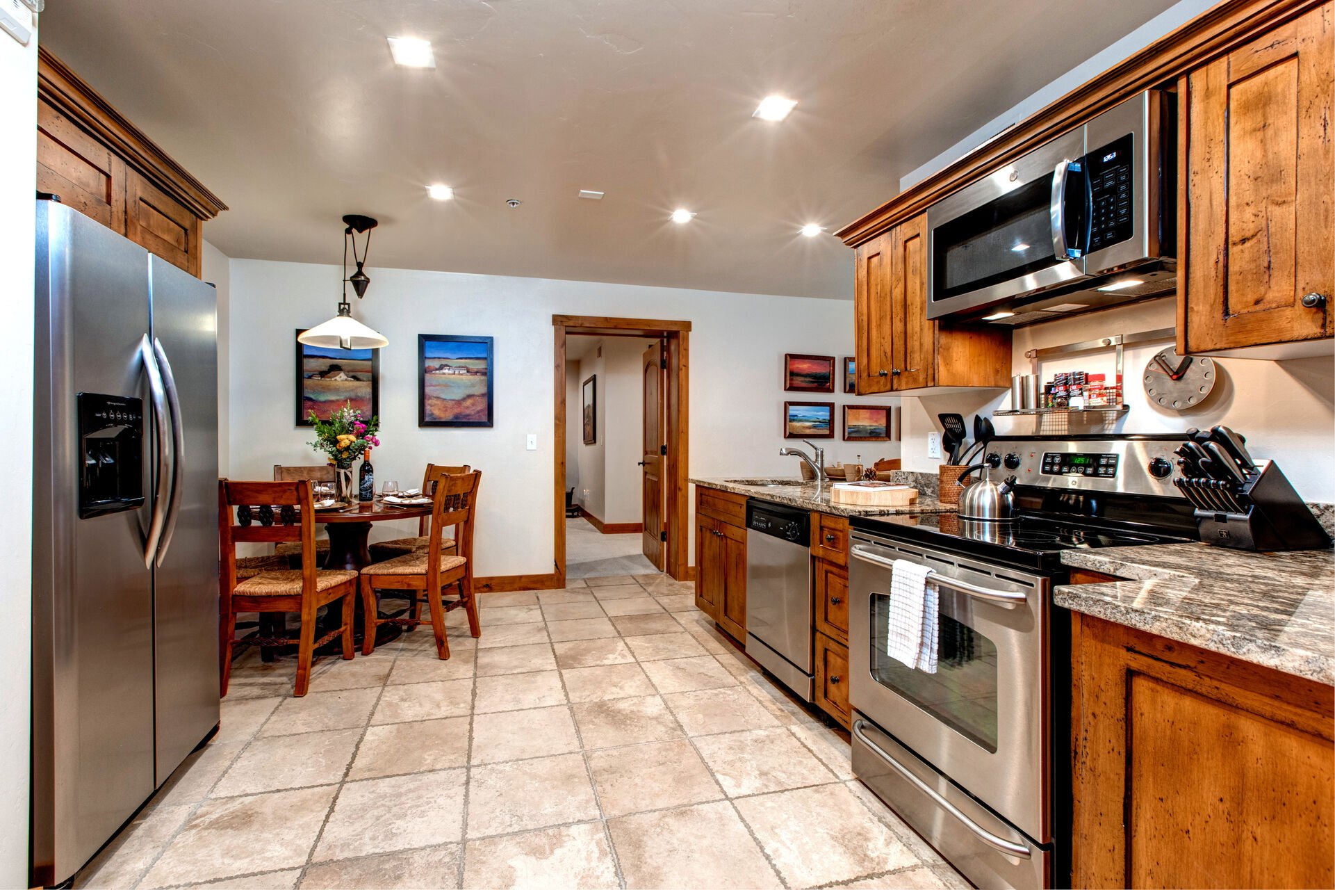Fully Equipped Kitchen Area with stainless steel appliances, ice maker, ample stone countertop space, dining table for 5, and bar seating for 2.