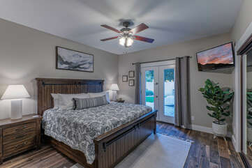 Bedroom 4 features a king bed, TV, ceiling fan and doors that access an outdoor walk along the side of the home.