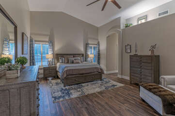 Elegant primary suite features tasteful decor, a king bed, en suite bath, walk-in closet, large TV and ceiling fan.