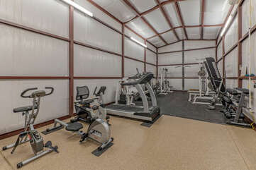 A large, air conditioned gym has workout equipment plus a ping pong table and corn hole game at the opposite end.
