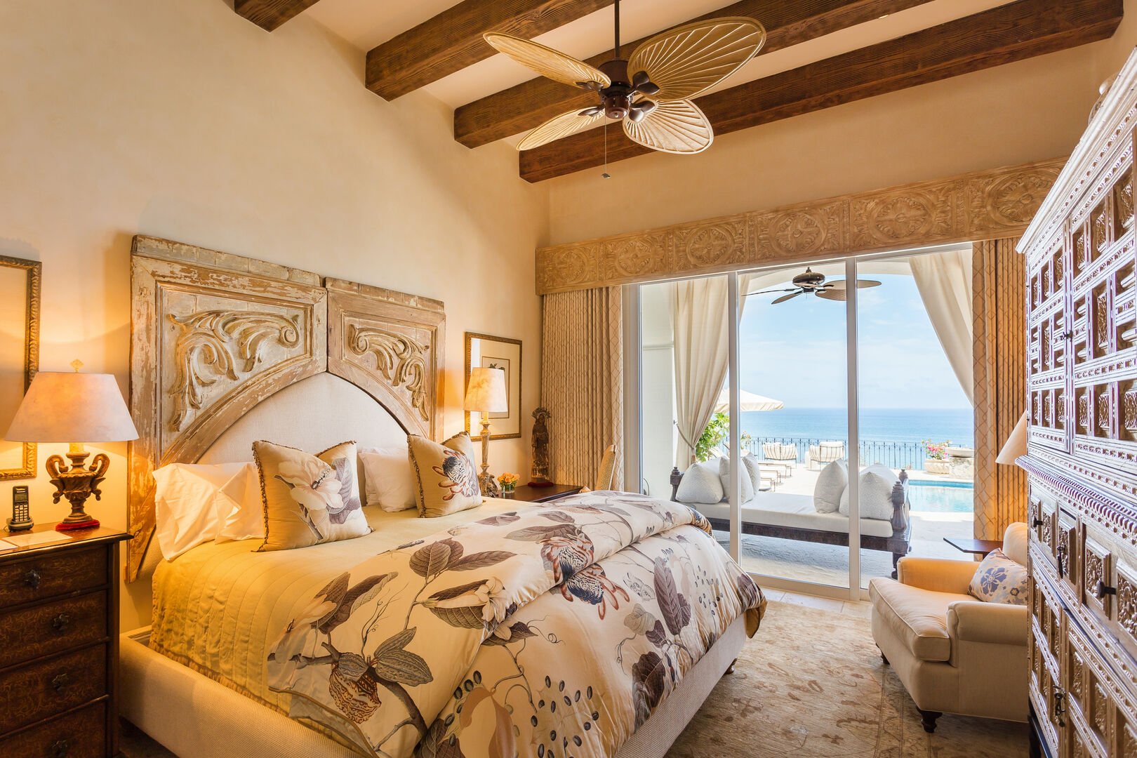Bedroom with access to a terrace with ocean views, a large bed, armoire, and ceiling fan