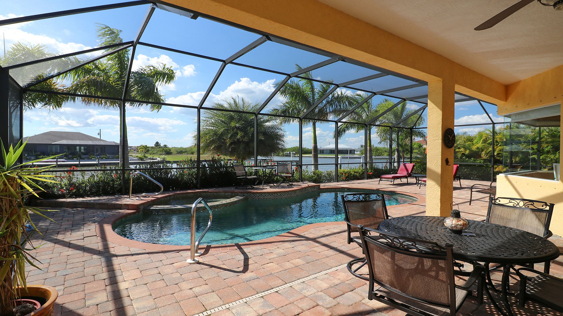 Gorgeous lanai with covered patio area with dining overlooking the pool and canal beyond