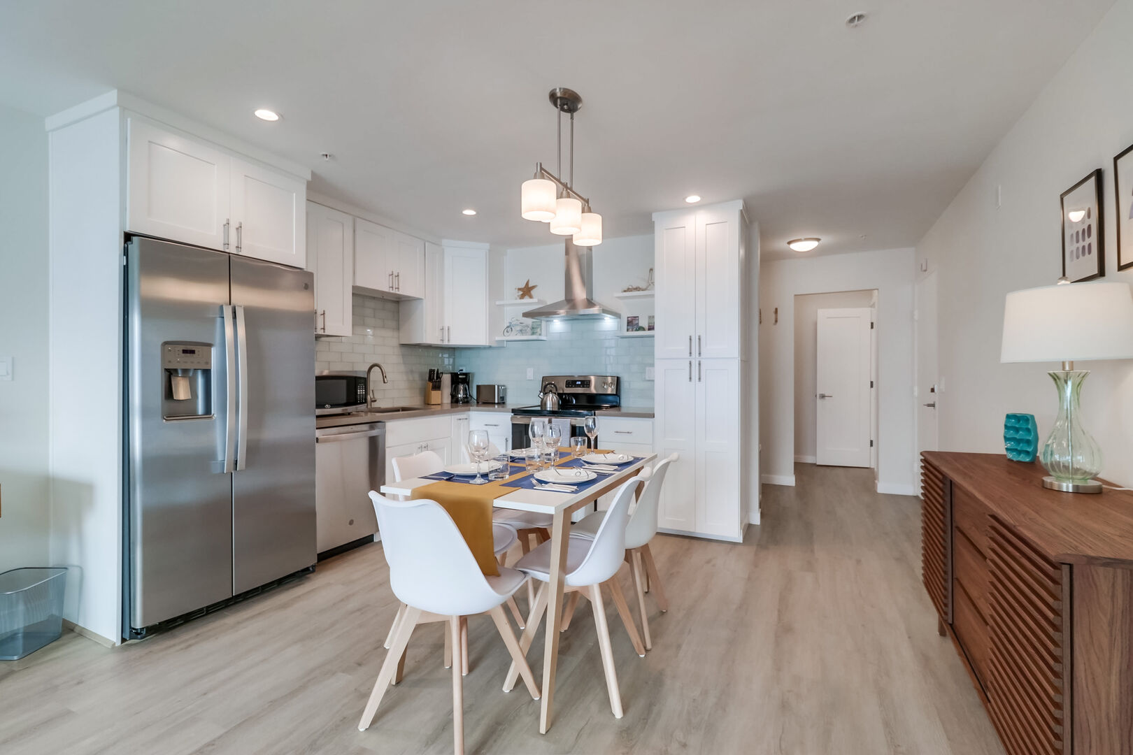 Open-style kitchen with modern, minimalist decor, stainless steel appliances and dining for 5 guests. The back foyer is the front entrance to the condo with the guest bedroom and separate bathroom