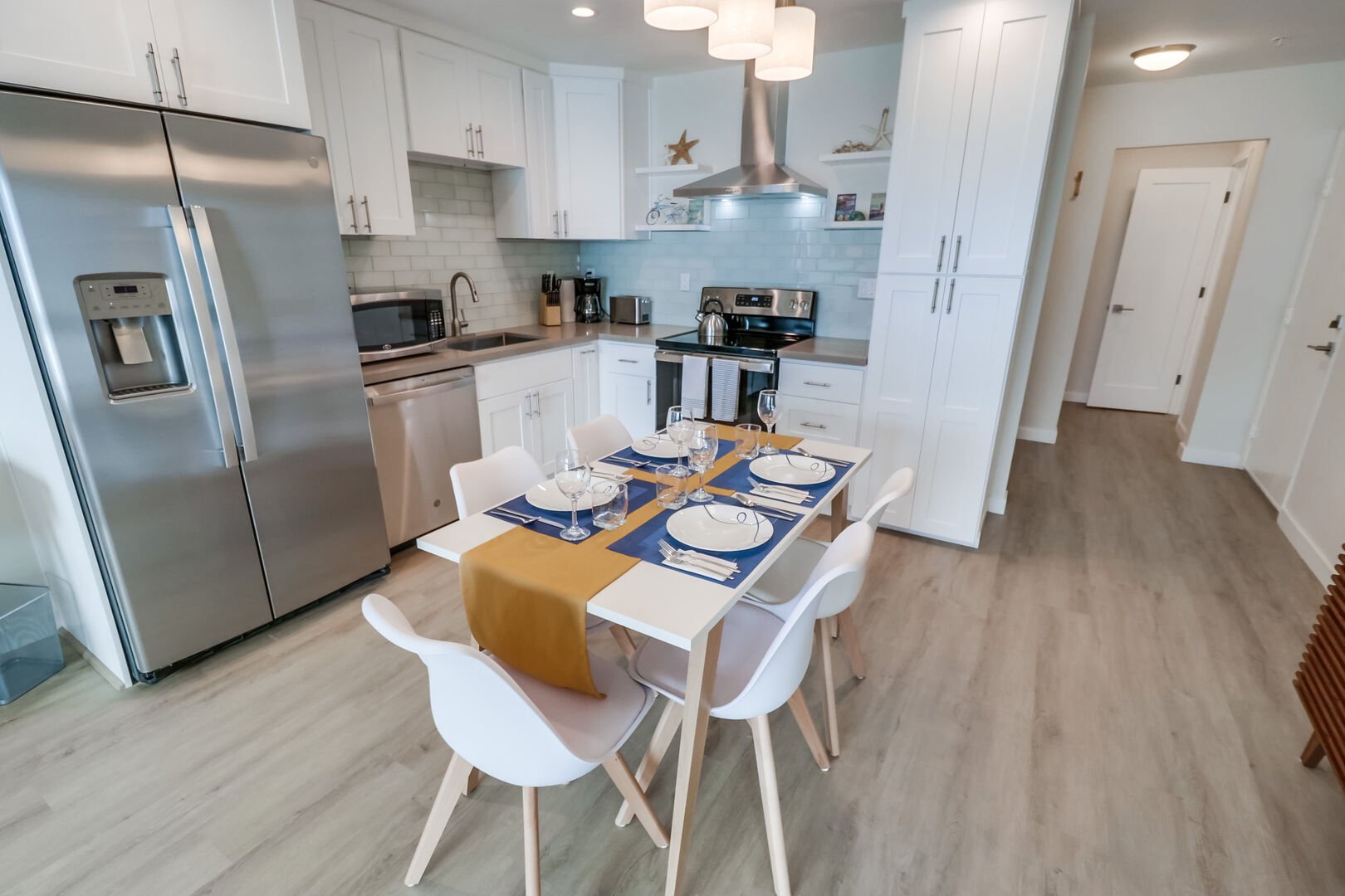 Open-style kitchen with modern, minimalist decor, stainless steel appliances, microwave, refrigerator and freezer with ice/water dispenser, toaster, standard coffee maker, electric stove top and oven, overhead lighting, dining for 5 guests and plenty of storage and pantry space