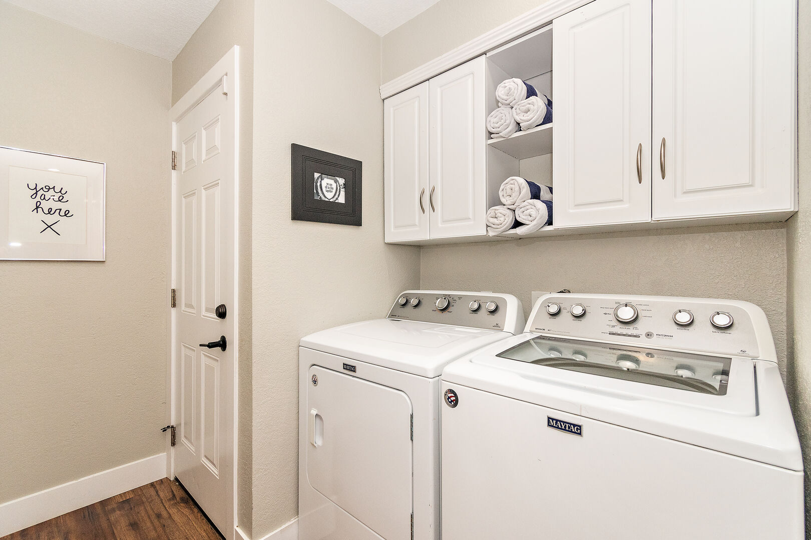 Fully equipped laundry room with washer, dryer, ironing board, iron, and laundry pods.