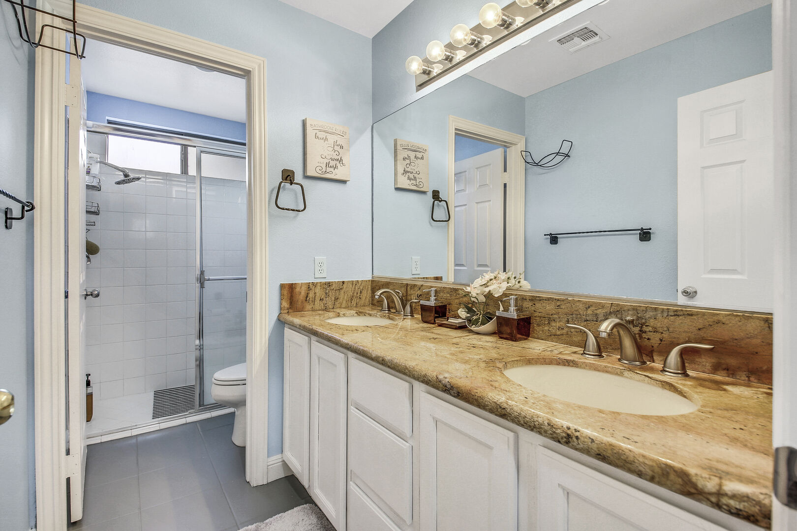 The downstairs hallway bathroom is located by the garage and features a tile shower and double vanity sinks.