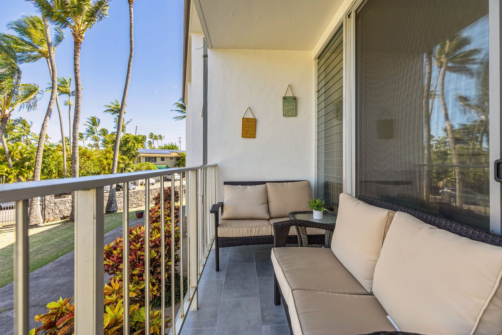 Balcony with patio furniture. Views of the backyard of the building and Kuau Cove with many palm trees