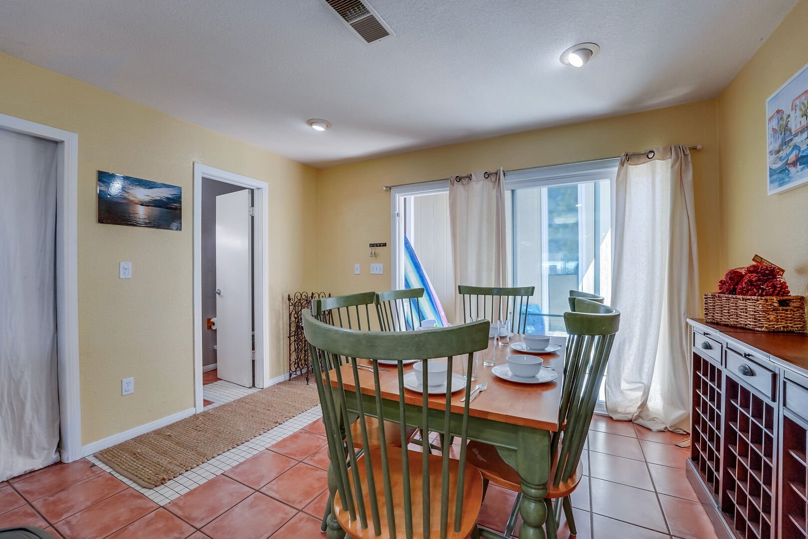 Kitchen area with dining table for 6 guests, half bathroom and back patio with washer/dryer and beach accessories