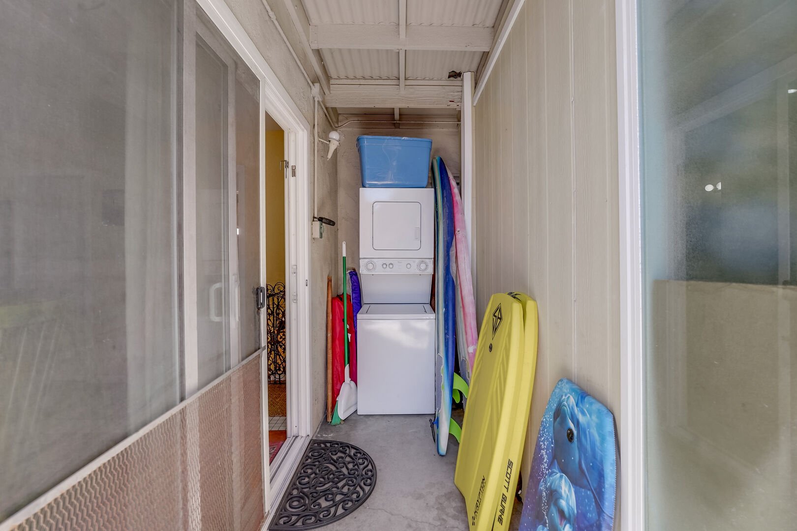 Side entrance to the ground level of the home to the kitchen, containing beach accessories and stackable washer/dryer