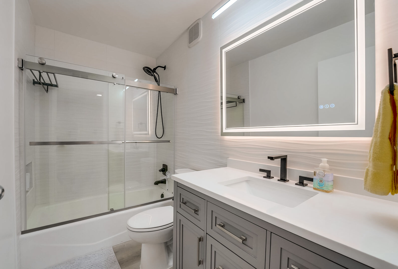 Spacious, bright and remodeled bathroom with shower/tub combo, toilet, vanity with ample storage space and LED dimmable smart mirror