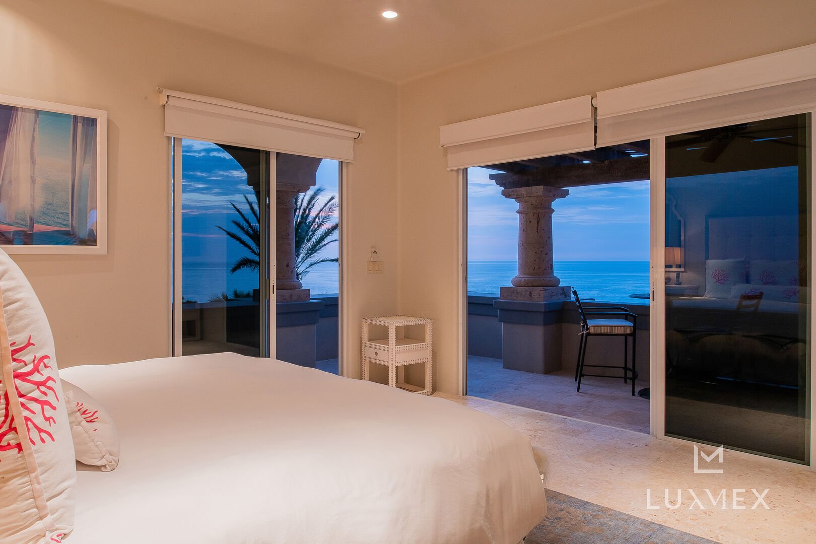 Views of the ocean form multiple large sliding glass doors in front of a bed.