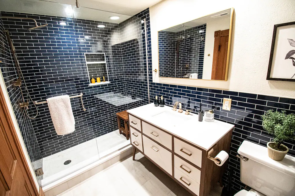 The stunning navy tiled bathroom features a rain head shower with teak bench.