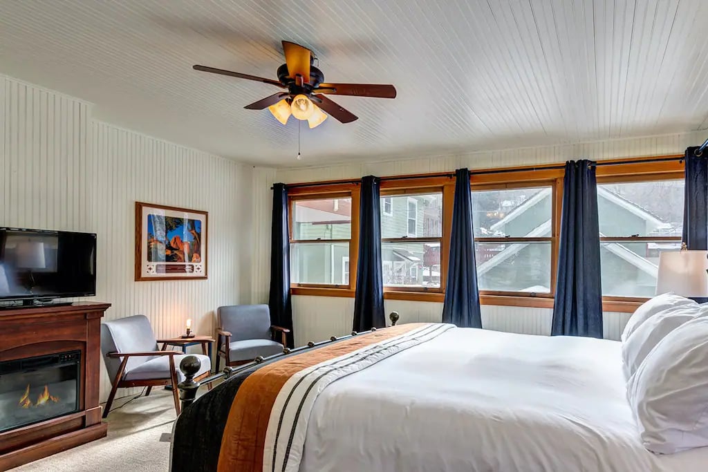 The Ruxton Room  in a large guest room format with a fireplace and tv at the foot of the plush king-size bed,