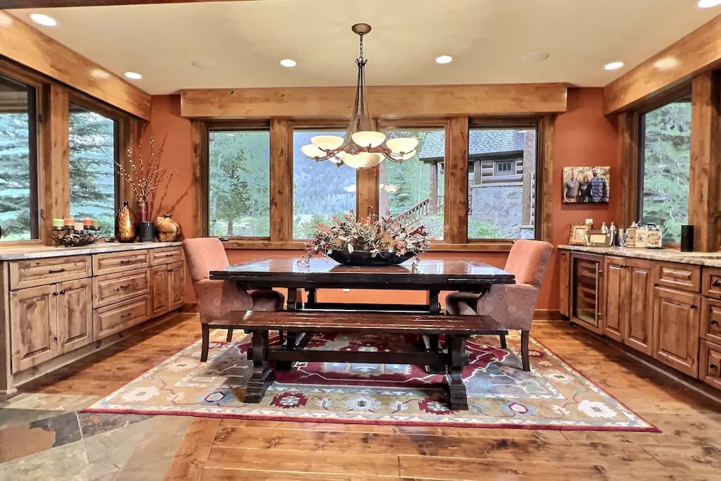 This dining room is surrounded in large picture windows showcasing the natural beauty outside the home. The dining room features a built in wine fridge, wet bar, and dining buffet with a full service set up for 12.