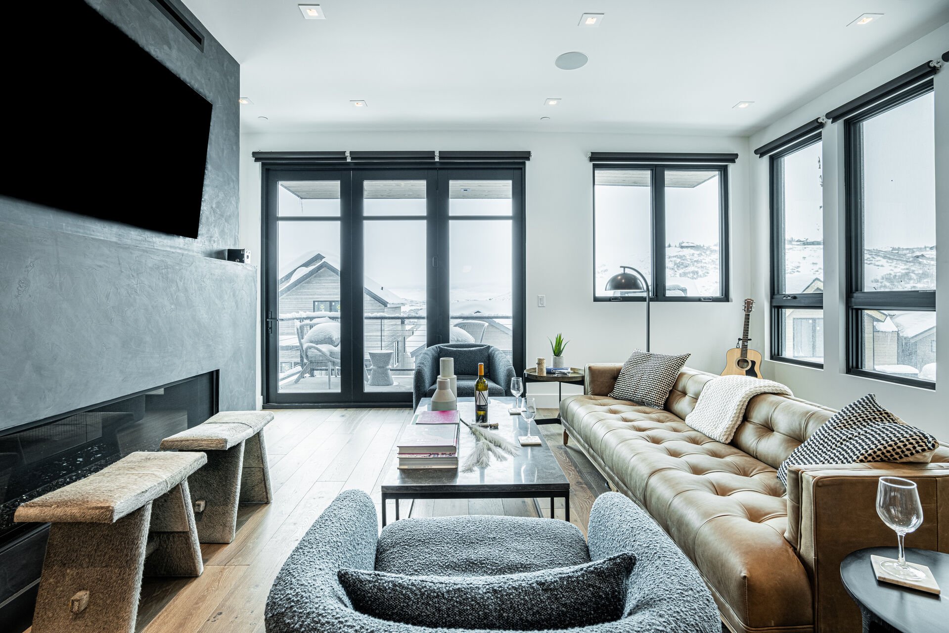 Main Level Living Room with contemporary leather sofa, plush arm chairs, elongated gas fireplace, and a 65” Smart TV, and access to one of the private decks