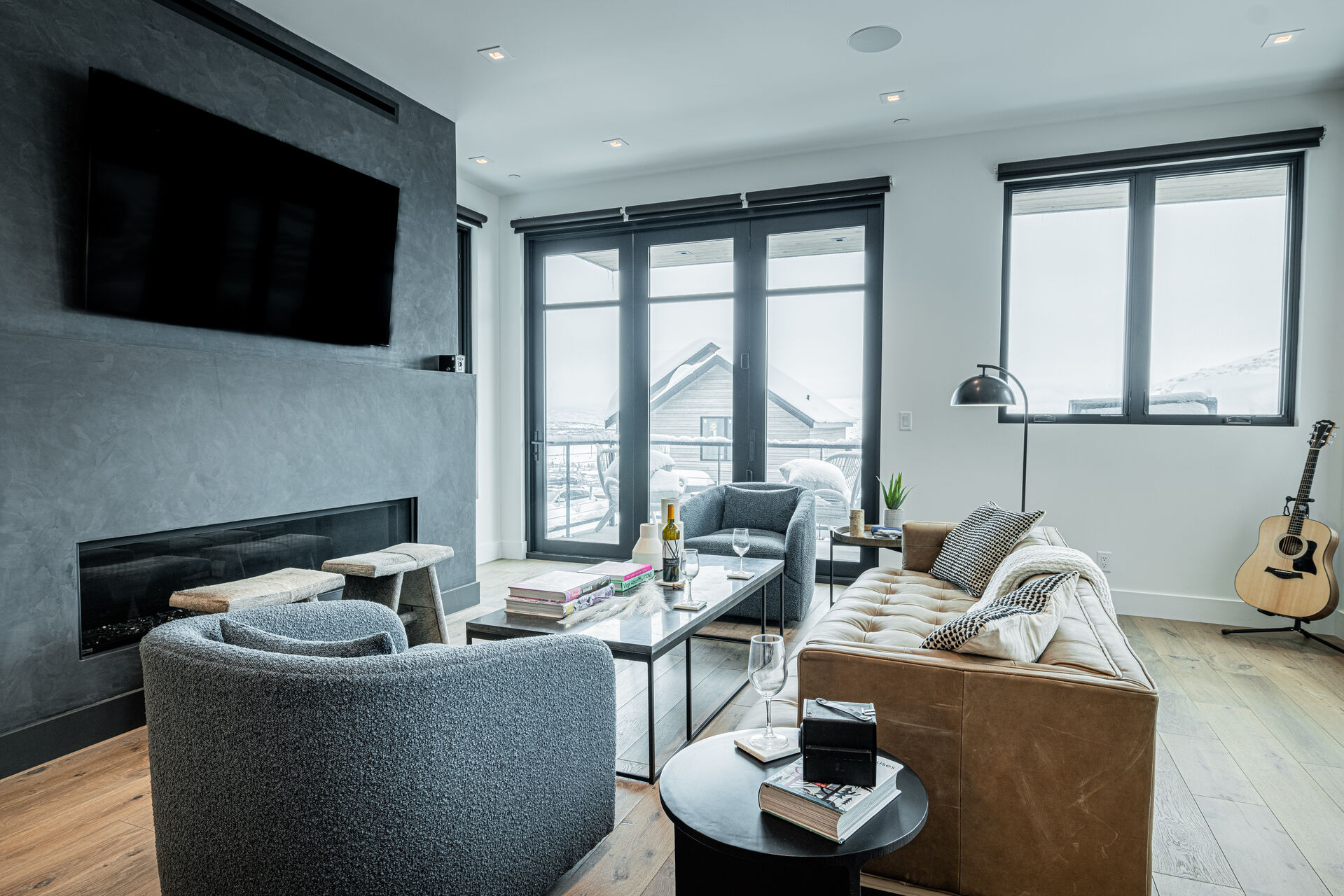 Main Level Living Room with contemporary leather sofa, plush arm chairs, elongated gas fireplace, and a 65” Smart TV, and access to one of the private decks