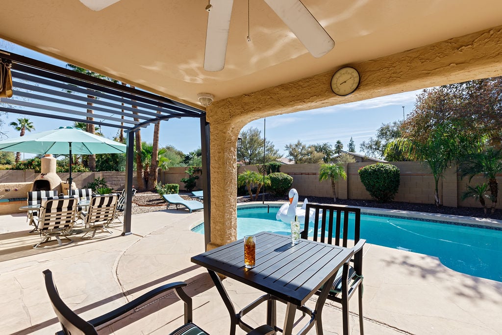 Large private yard with sparkling pool, diving board, covered patio with outdoor dining area, sun loungers, and outdoor fire place.
