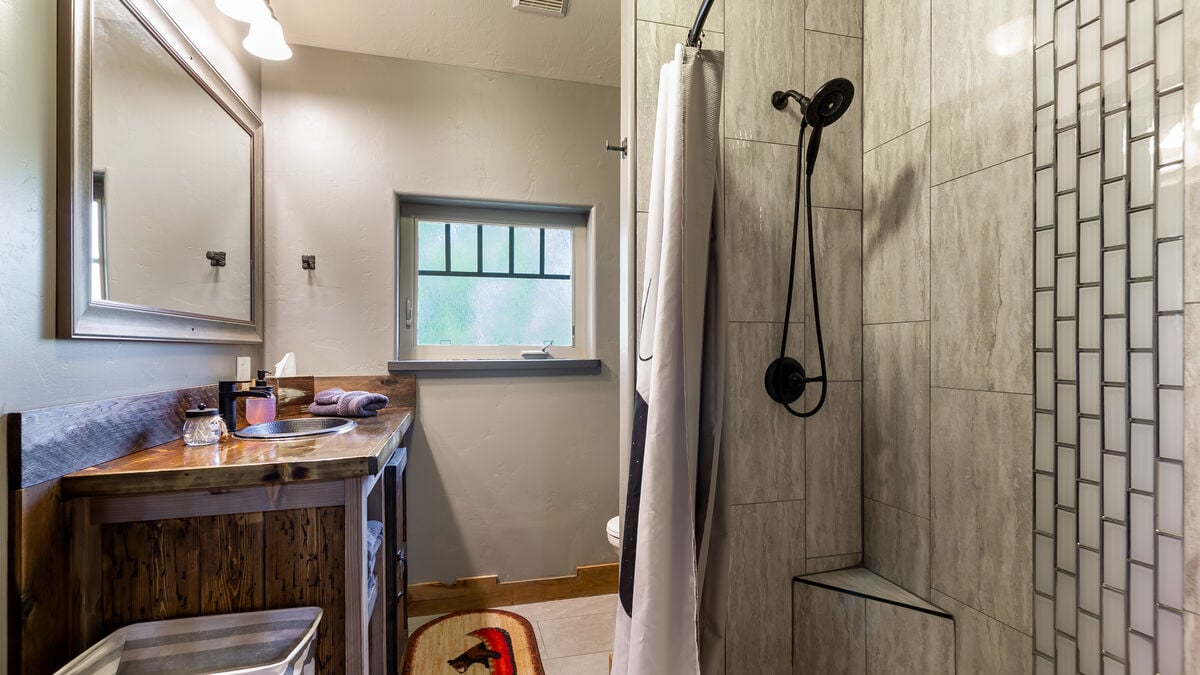 Enjoy the warm, rustic ambiance of this remodeled bath featuring a custom-made oversized vanity, a beautiful step-in tiled shower featuring a stunning waterfall design, a convenient corner bench, and a handy handheld showerhead. 
(Room 5)