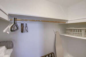 Shared walk-in closet with iron, ironing board, hangers, extra linens and towels and laundry supplies
