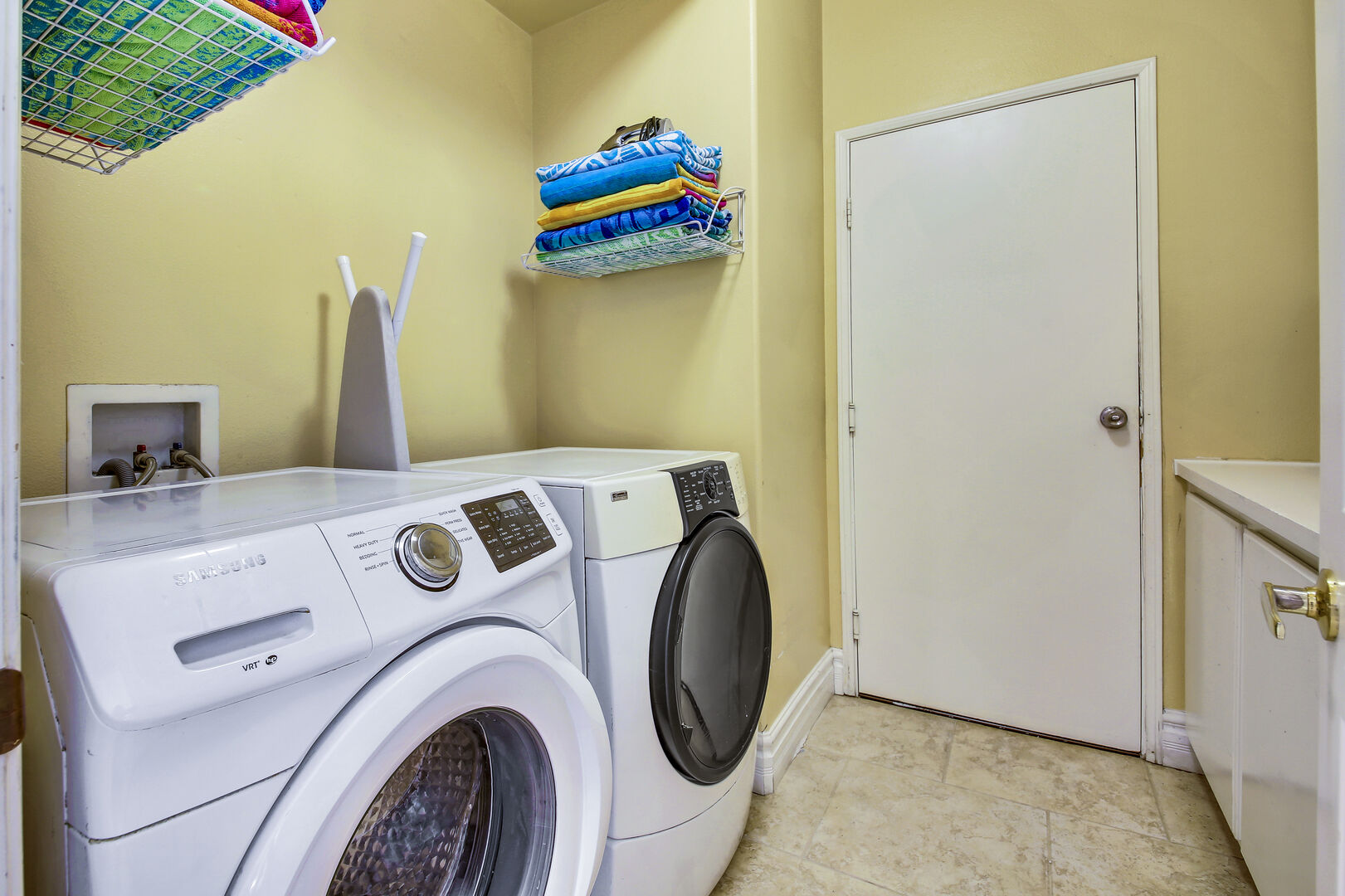 Fully equipped laundry room with washer, dryer, iron, ironing board, and laundry pods.