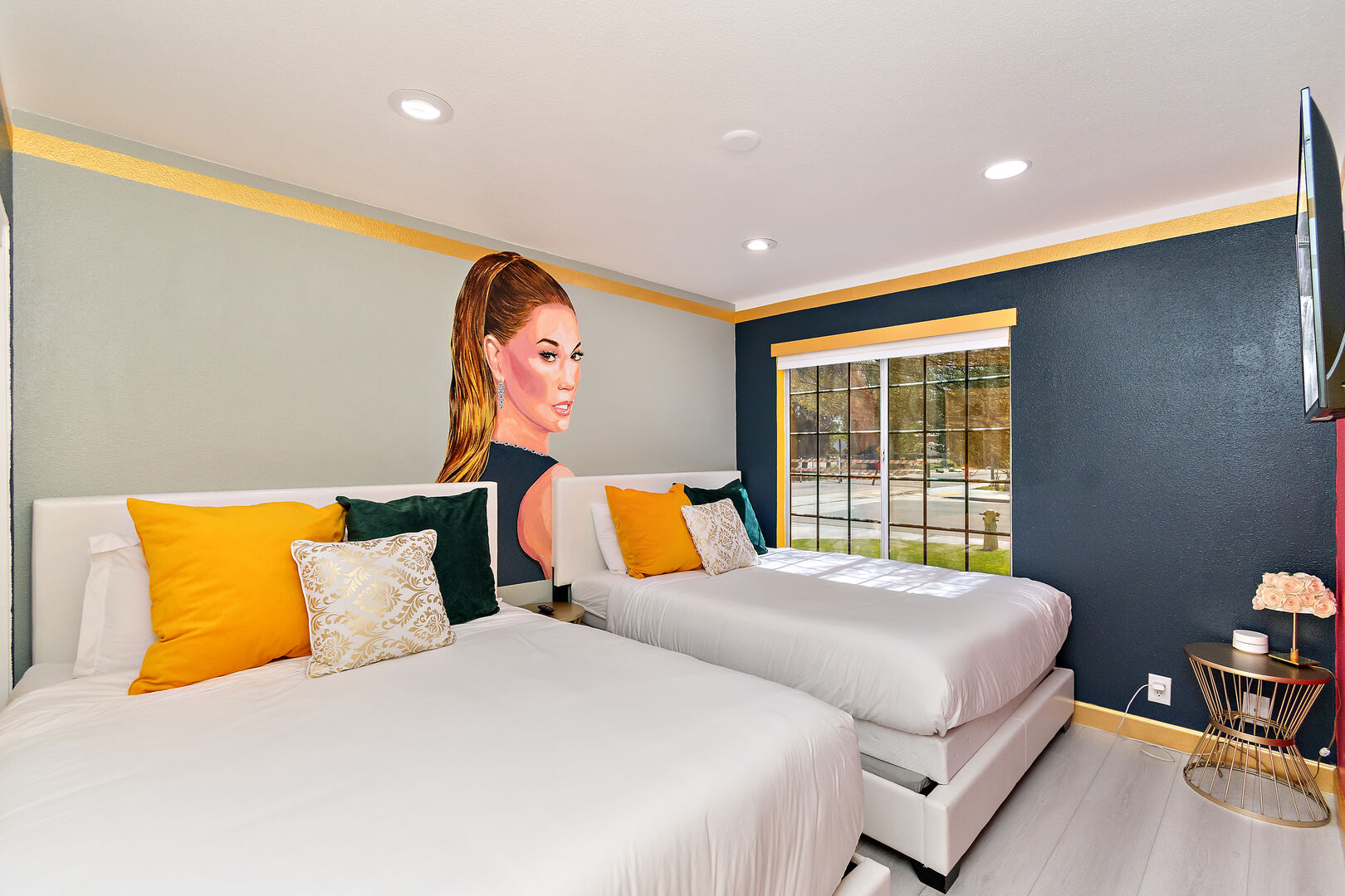 Bedroom 3 is located next to bedroom 4 and features two Queen-sized Beds, a 40-inch TCL with Roku Smart television, and a Jennifer Lopez mural.