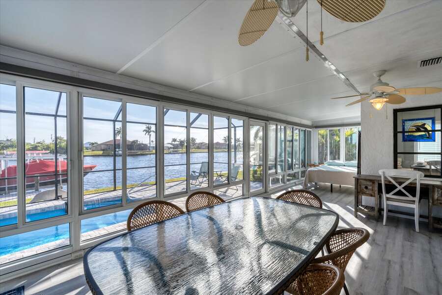 Sunroom overlooking pool and canal with outdoor dining, desk, and queen bed. Nook with queen  bed has a room divider for privacy
