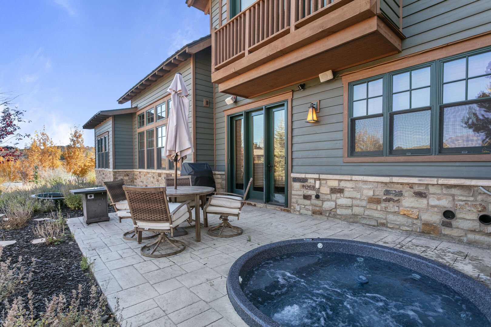 Charming patio with private hot tub, outdoor dining table, and BBQ grill.