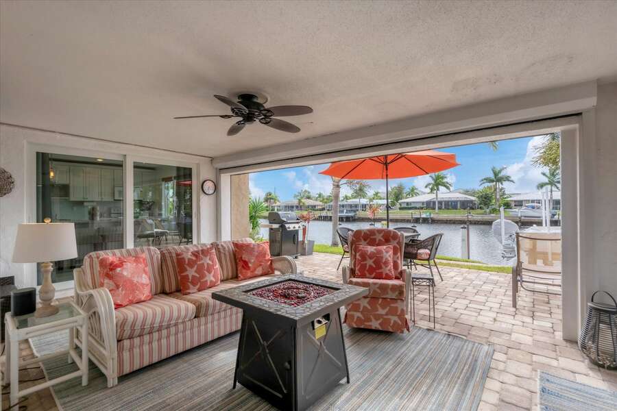 Spacious outdoor area with hot tub, conversation seating area with fire pit coffee table, and dining table overlooking the water. Lanai also features a propane BBQ grill