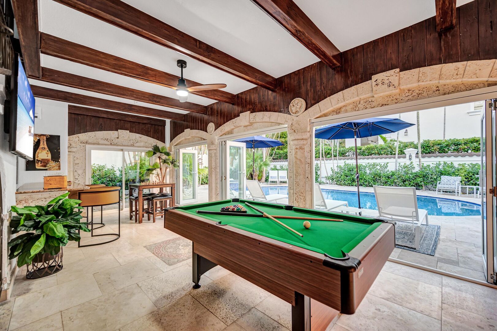 The covered patio, featuring a bar area with a pool table, boasts floor-to-ceiling windows providing seamless access to the heated pool.