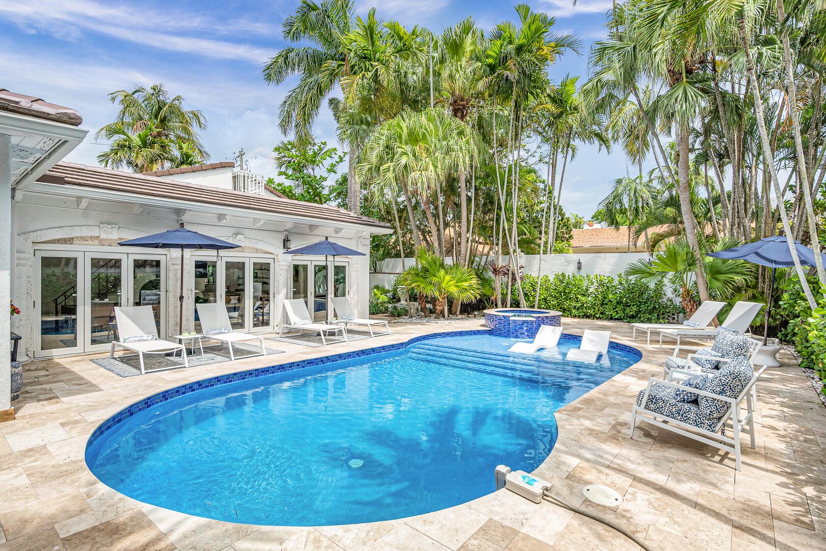 The heated pool and hot tub in the lush tropical garden with access to the covered patio, featuring a pool table and a bar.