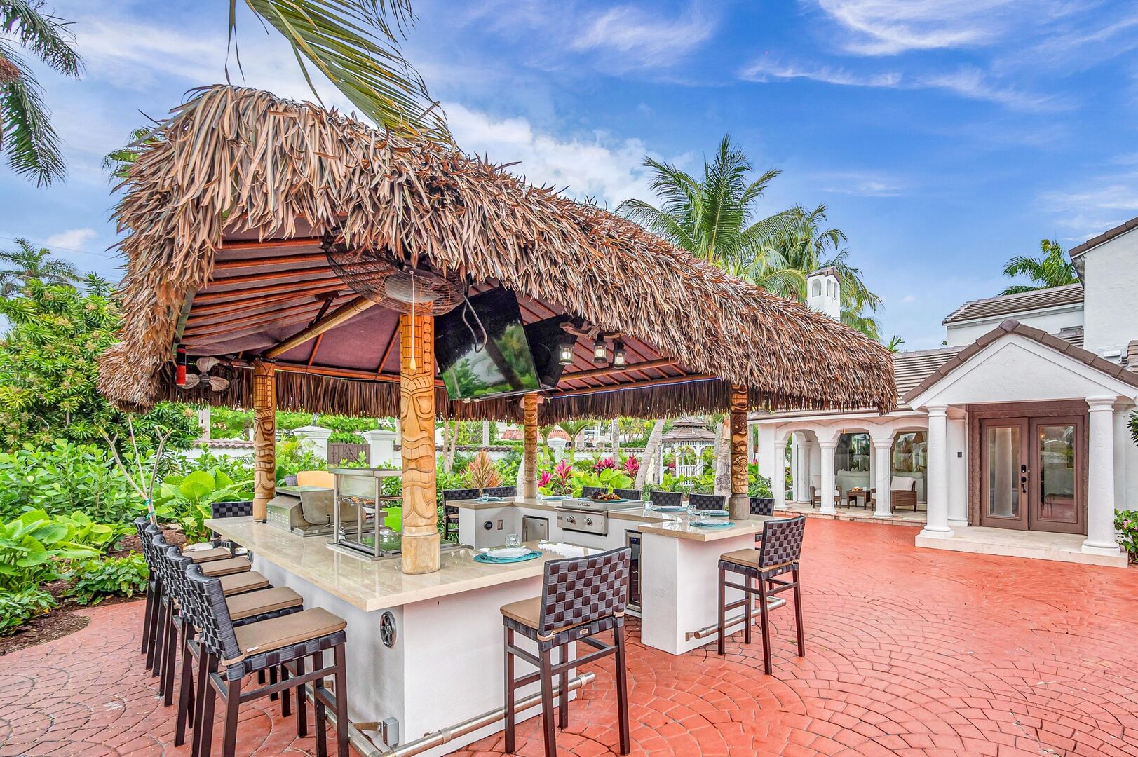 The tiki outdoor kitchen with wrapped around bar seating features two TVs and a bbq.