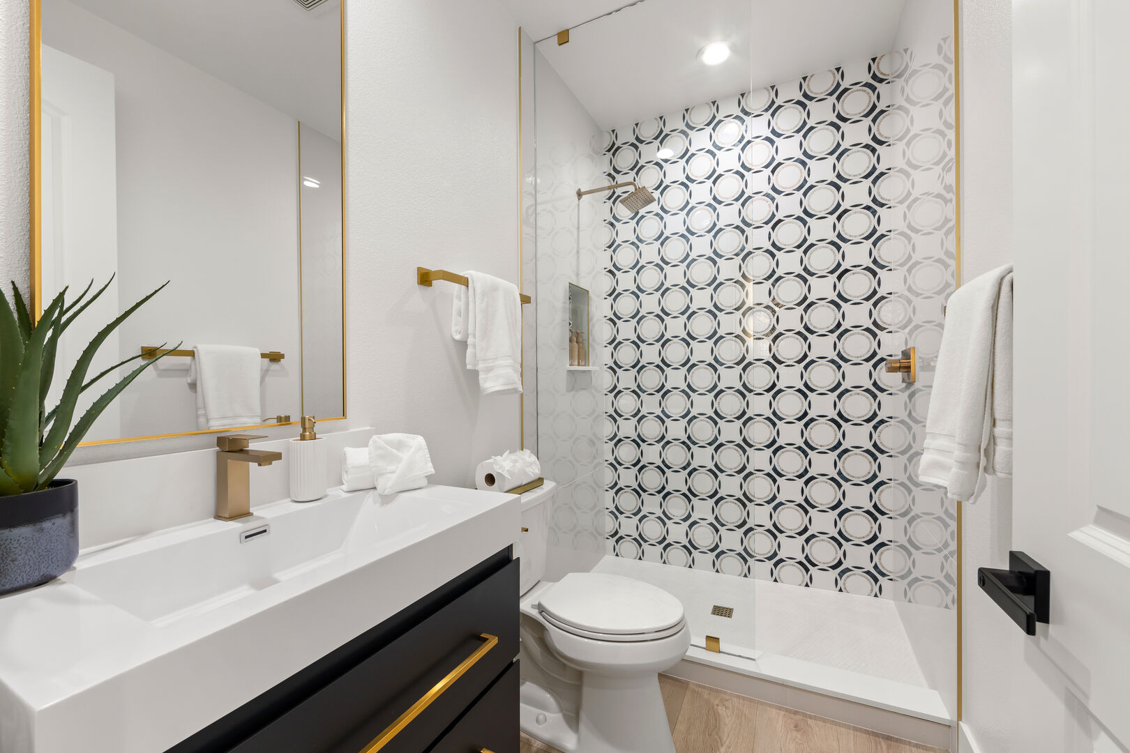 Hallway Bathroom Four is next to the laundry room and features a step-in tile shower with a decorative vanity sink. This bathroom features a fun geometric tile shower and gold accent hardware.