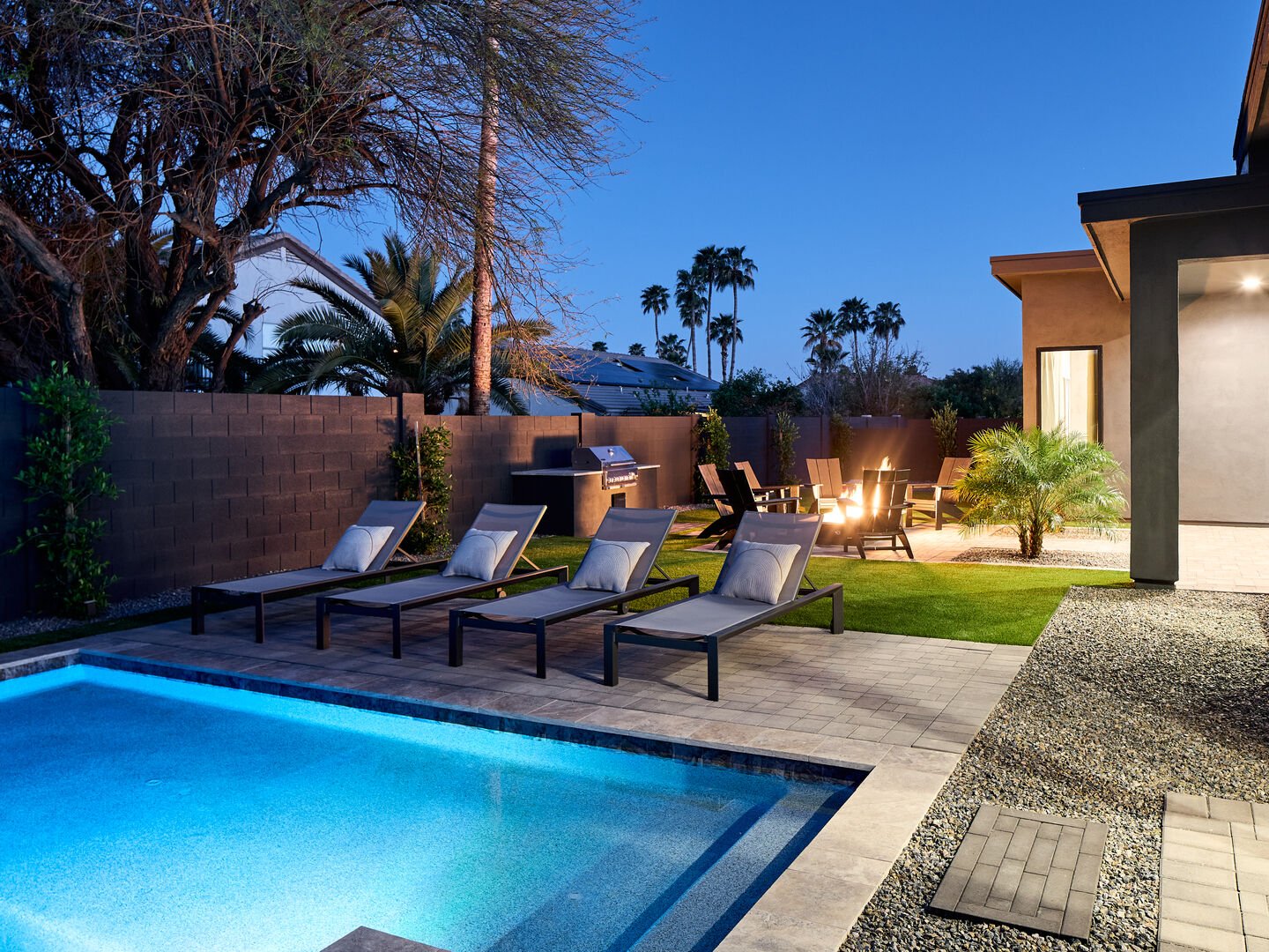 Resort-like backyard with a covered patio offering outdoor dining, a sparkling blue heated pool with sun loungers, yard games, a BBQ grill and a fire pit.