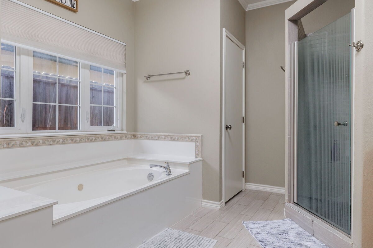 Step into comfort with this elegant bathroom featuring a large soaking tub, perfect for unwinding after a long day, and a separate glass-enclosed shower.