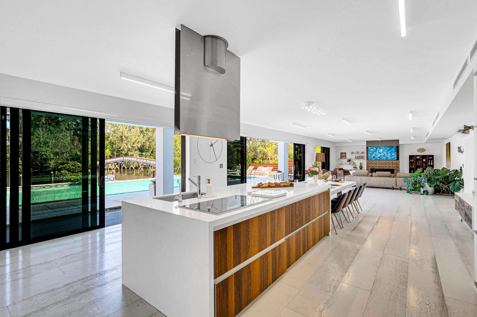 The kitchen is lined with sliding floor-to-ceiling windows, offering waterfront views and seamless access to the pool and outdoor kitchens.