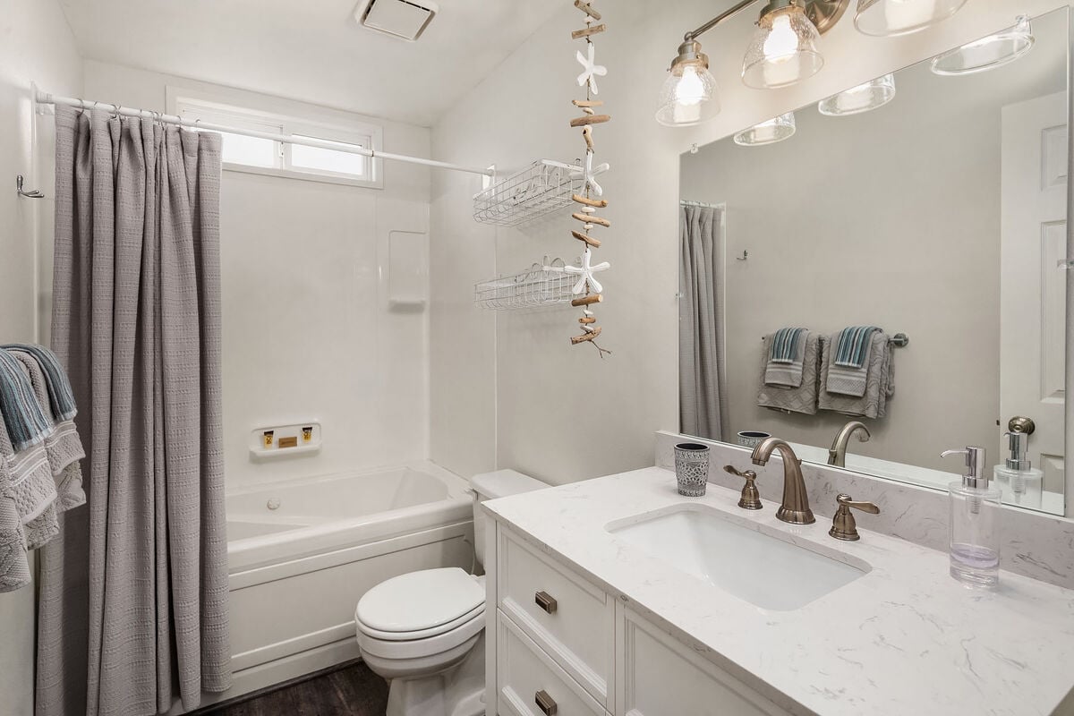 A main bathroom is positioned between the second and third bathrooms. It features a shower over a jetted bathtub, a toilet, and a vanity.