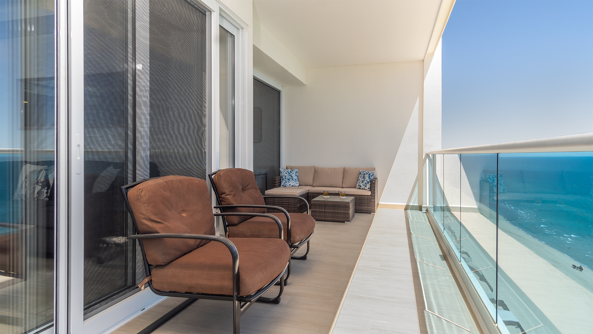 long balcony has two easy chairs, a sofa area and dining table