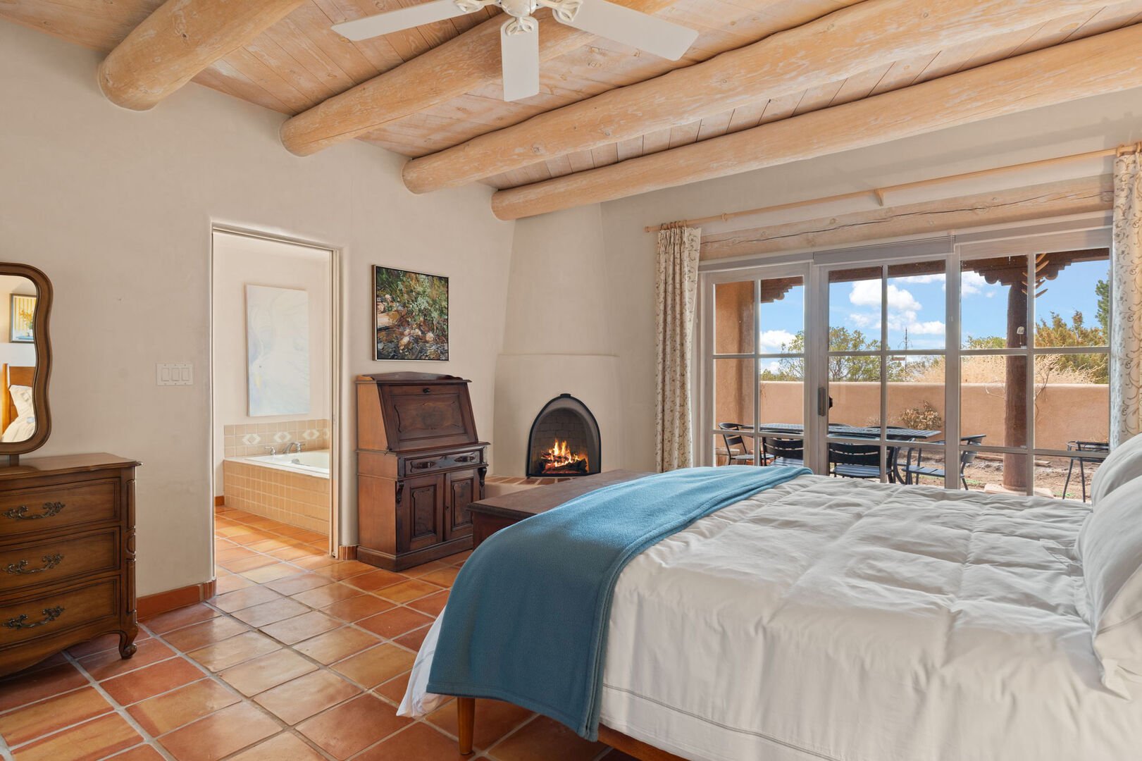 Retreat to the primary bedroom oasis with a plush king bed, a charming kiva fireplace (for decoration/not usable), tall white-washed lodge-pole ceilings, and sliding glass doors opening to a private backyard retreat.