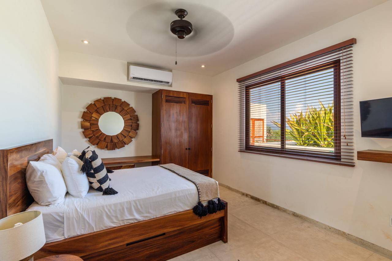This chic bedroom offers a cozy retreat with rustic wood details, handcrafted decor, and lush tropical garden views.