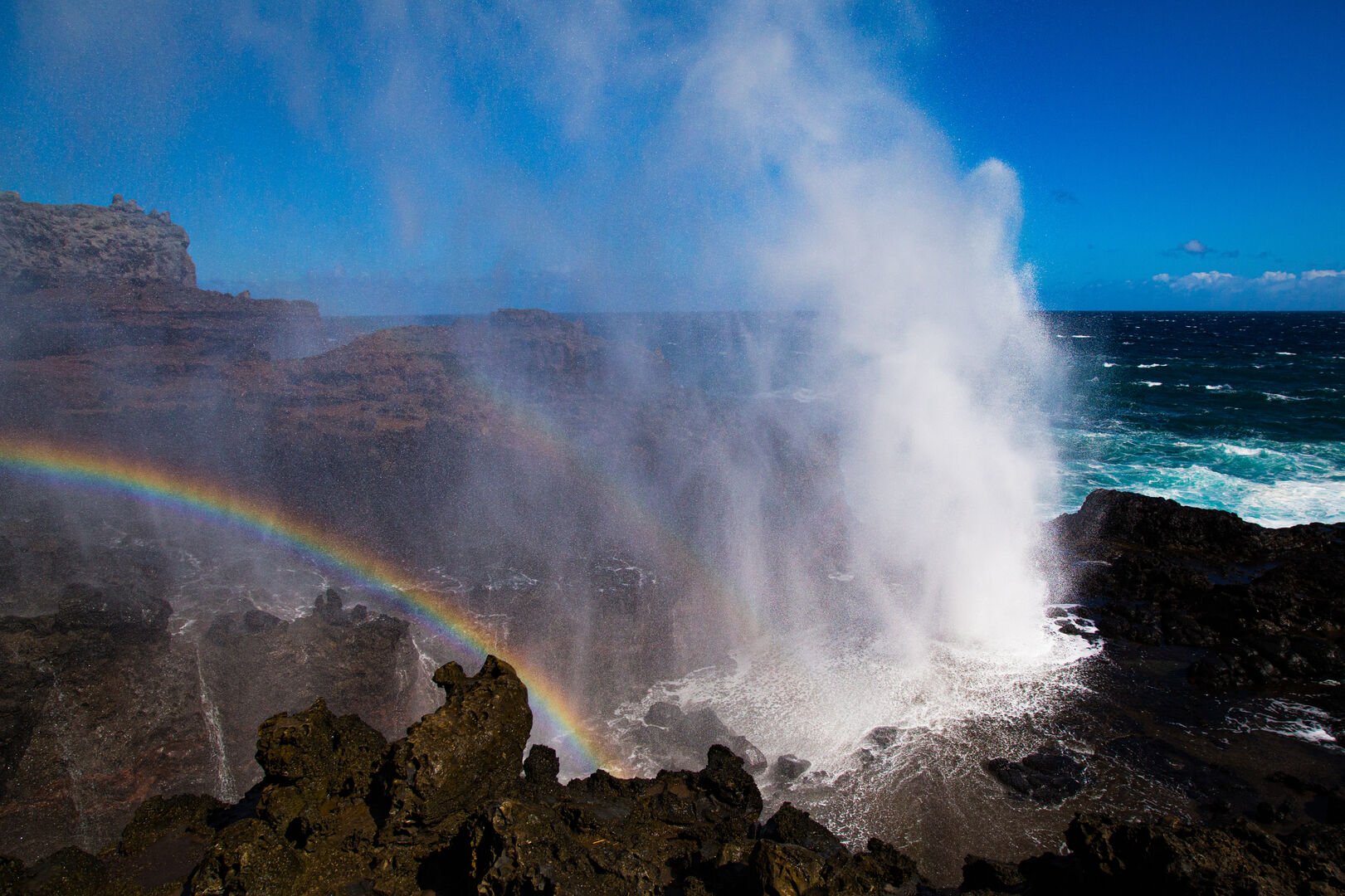 Marvel at the Nakalele Blowhole, a natural wonder on Maui's coastline, where ocean mist creates vibrant rainbows in the midday sun.